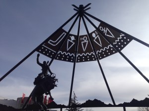 Bronc Twister sculpture with metal teepee in background with symbols of first people nations that participate in the stampede.